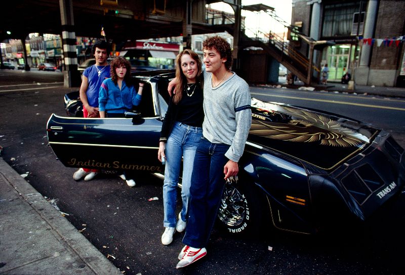 Image of 1980's Dateable couple and their friends leaning on expensive car.